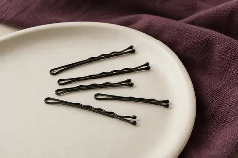 Mini épingles à cheveux noires en métal, ondulées et à embouts arrondis, disposées sur une céramique mate