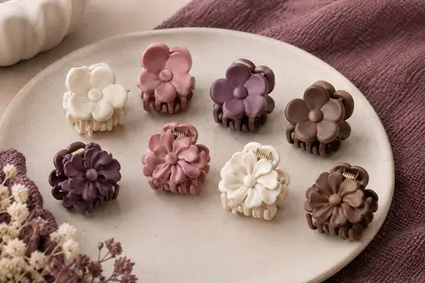 Huit mini pinces à griffes en plastique, aux formes florales et coloris assortis, posées sur une céramique mate.