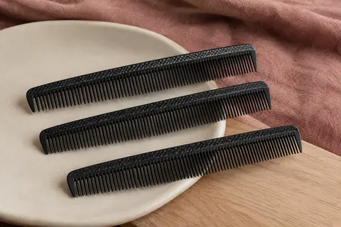 Trois peignes de coupe noirs en fibre de carbone posés sur un support en céramique mate