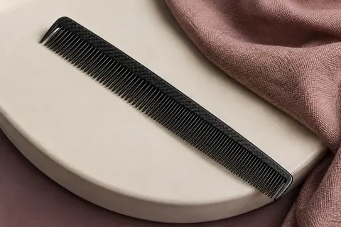 Peigne de coupe noir en polycarbonate et fibre de carbone posé sur un support en céramique mate.