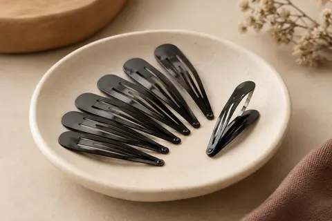 Lot de barrettes noires en métal à fermeture pression disposées sur une coupelle en céramique mate