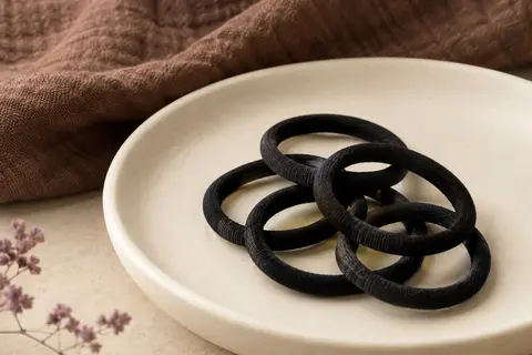 Élastiques circulaires noirs en coton disposés sur une céramique mate et un tissu brun texturé