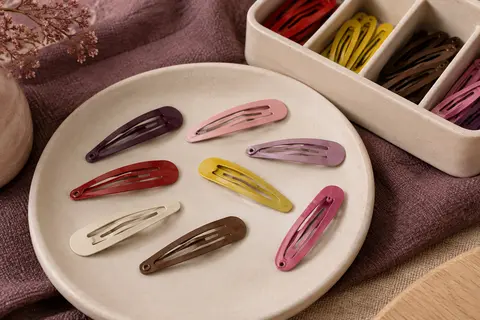 Barrettes pression métalliques multicolores disposées près de leur étui de rangement compartimenté