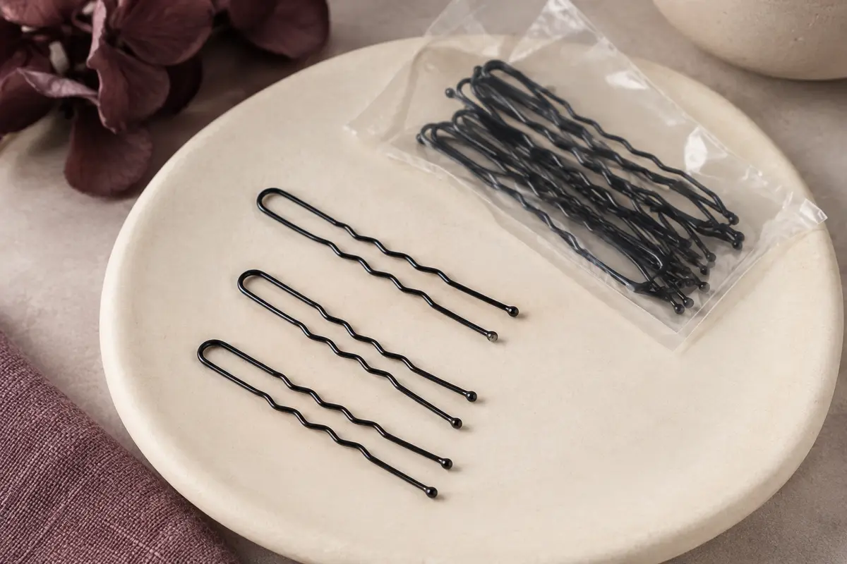 Épingles à cheveux en U noires et ondulées disposées sur un support en céramique mate