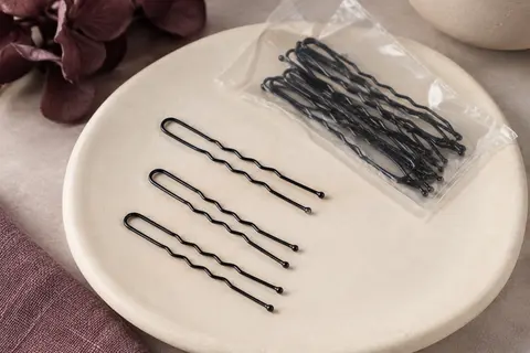 Épingles à cheveux en U noires et ondulées disposées sur un support en céramique mate