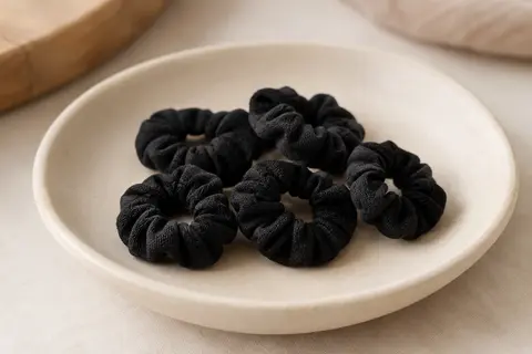 Mini chouchous noirs en coton disposés sur une coupelle en céramique mate