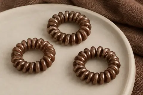 Trois élastiques cheveux spirales en résine bronze disposés sur une céramique mate.