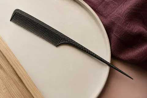 Peigne à queue noir en fibre de carbone posé sur une céramique mate, avec ses dents fines visibles
