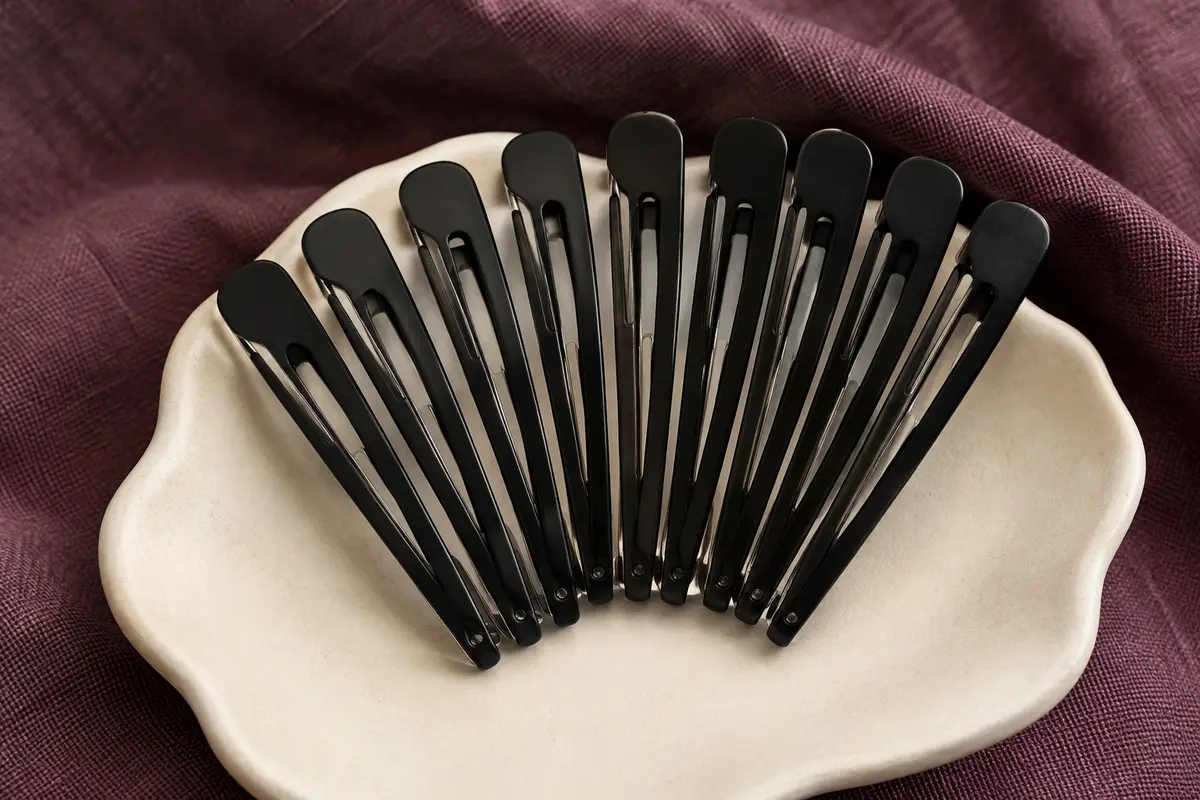 Lot de pinces à cheveux noires sans pli disposées sur un support en céramique mate