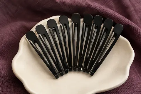Lot de pinces à cheveux noires sans pli disposées sur un support en céramique mate