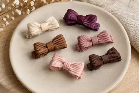 Petites barrettes à nœud en gros-grain multicolore disposées sur un support en céramique mate.