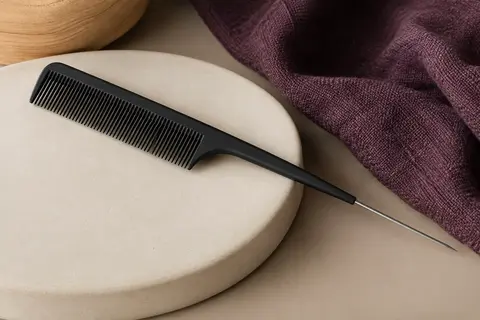 Peigne à crêper noir à dents fines avec pique métallique posé sur un support crème