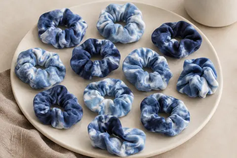 Lot de chouchous tie-dye bleus en tissu doux, disposés sur un support en céramique mate