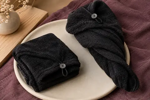 Deux serviettes turban noires en microfibre, avec boucle et bouton, présentées sur un support crème.