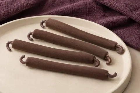 Quatre bigoudis flexibles bruns avec crochets, disposés sur un support en céramique mate.