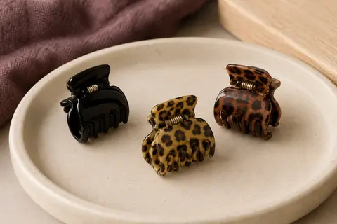 Trois petites pinces à cheveux à griffes, noire et à motifs léopard, posées sur un support en céramique mate.