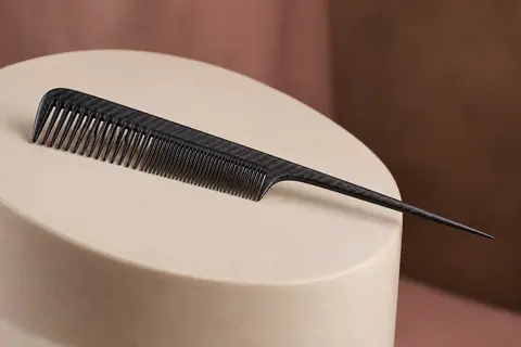 Peigne à queue noir en fibre de carbone, avec dents larges et fines, posé sur un support en céramique mate.