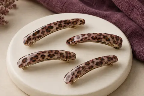Quatre pinces plates incurvées en résine au motif léopard, disposées sur un support en céramique mate.