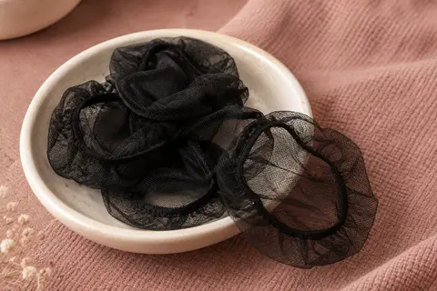 Filets à chignon noirs en maille fine et extensible, disposés sur une coupelle en céramique crème.