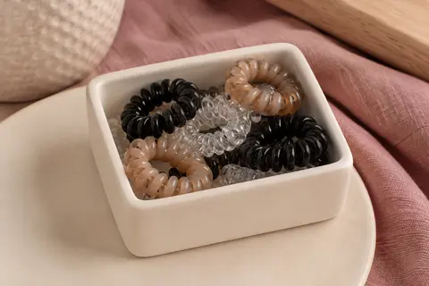 Élastiques cheveux spiralés noirs, café clair et transparents disposés avec leur boîte de rangement.
