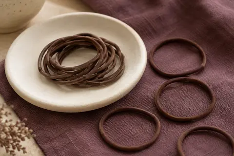 Lot d’élastiques marron fins et sans métal disposés sur une céramique mate avec un tissu prune.