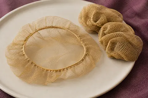 Filets à chignon en nylon doré à maille fine et bord élastique, posés sur une céramique mate