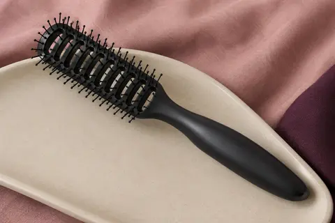 Brosse de brushing noire à tête ventilée et picots flexibles posée sur un support en céramique mate