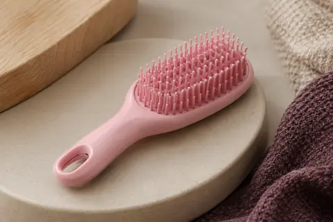 Brosse démêlante compacte rose posée sur une céramique mate, avec ses picots flexibles visibles.