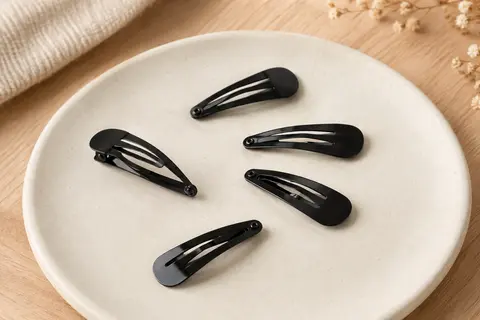 Petites barrettes métalliques noires disposées sur un support en céramique mate et en bois clair