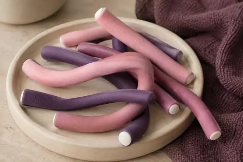 Bigoudis flexibles en mousse rose et violet de plusieurs diamètres, disposés sur un support en céramique