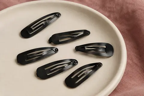 Barrettes à clip compactes en métal noir disposées sur un support en céramique mate crème.