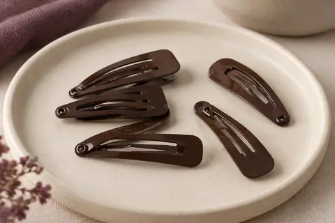 Lot de barrettes métalliques marron foncé à clipser, disposées sur un support en céramique mate