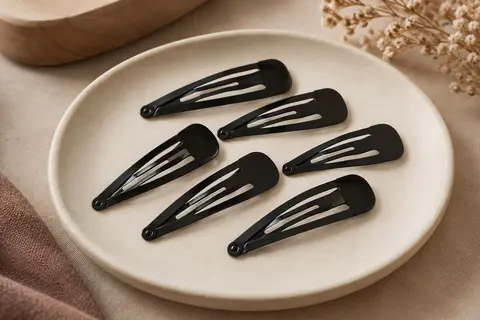 Lot de barrettes plates en métal noir disposées sur un support en céramique mate